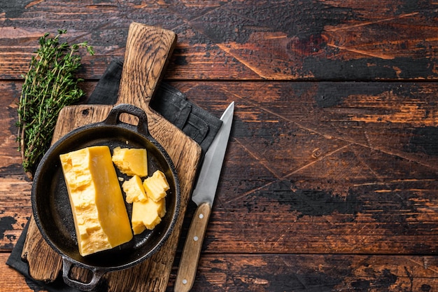 Photo parmesan hard cheese piece in a pan. dark wooden background. top view. copy space.