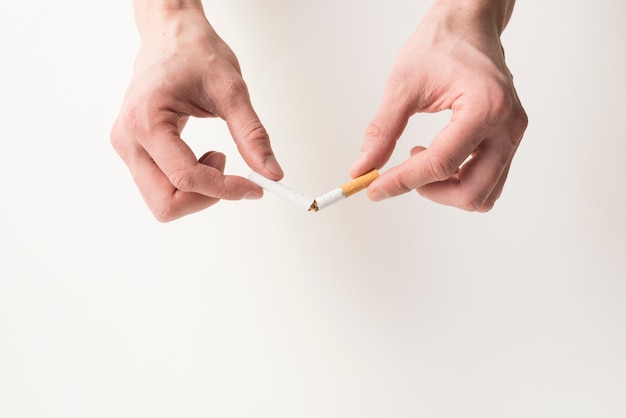 Person's hand breaking cigarette on white background