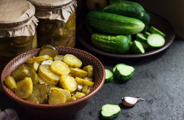 Photo pickled cucumber salad in a bowl and jars on black background