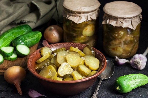 Photo pickled cucumber salad in a bowl and jars on black background