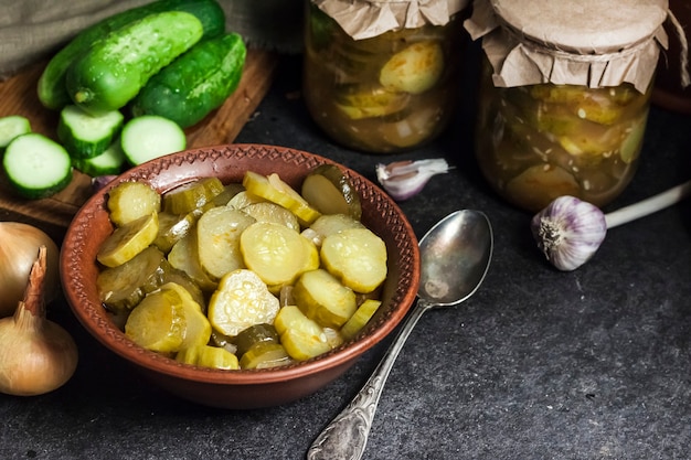 Photo pickled cucumber salad in a bowl and jars on black background