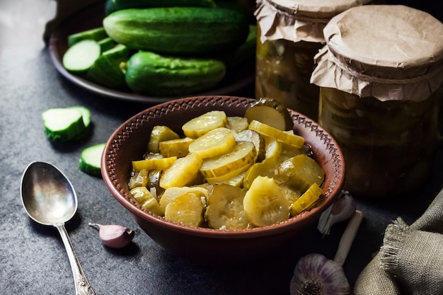 Photo pickled cucumber salad in a bowl and jars on black background