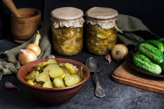 Photo pickled cucumber salad in a bowl and jars on black background