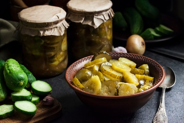 Photo pickled cucumber salad in a bowl and jars on black background