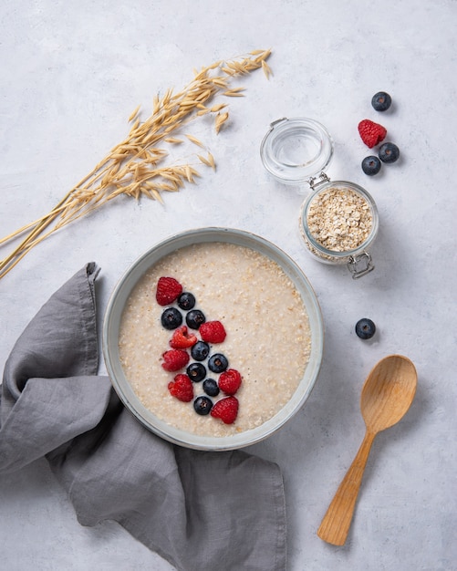 Photo plate of oatmeal porridge with blueberries and raspberries and textile napkin on white table. top view. healthy breakfast, concept