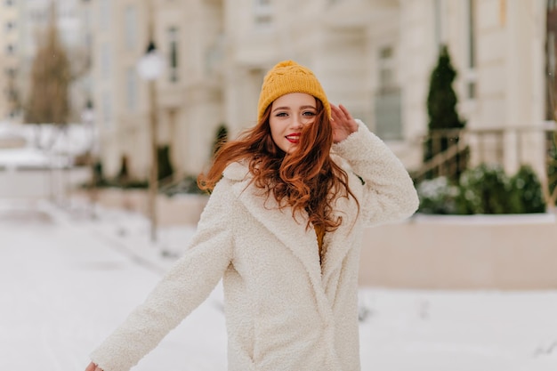 Playful ginger girl in knitted hat looking to camera Outdoor portrait of young woman posing in winter