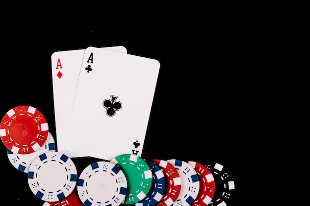 Poker chips and two aces playing cards on black surface