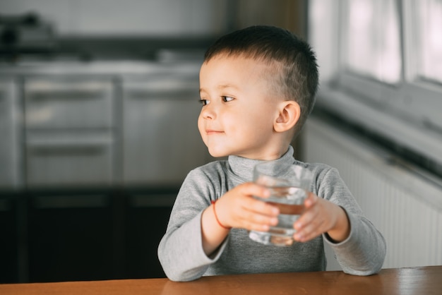 Portrait of a boy drinking a glass of water,happy in the kitchen very sweet