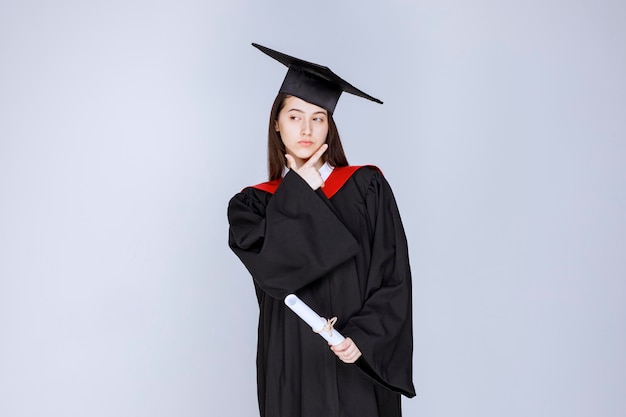 Portrait of graduate student in gown holding diploma and standing. High quality photo