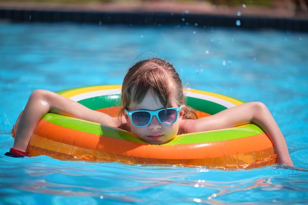 Portrait of happy child girl relaxing in inflatable circle in swimming pool on sunny summer day during tropical vacations Summertime activities concept