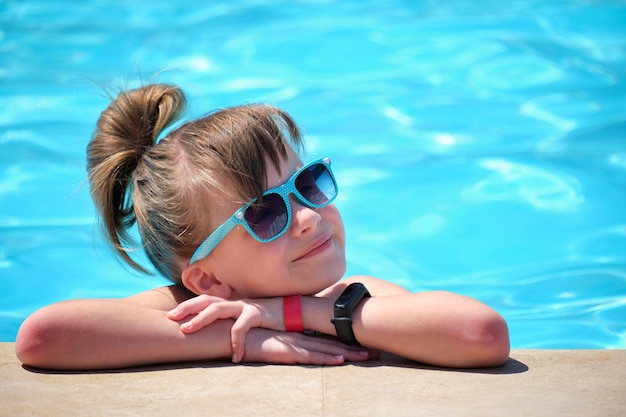 Portrait of happy child girl relaxing on swimming pool side on sunny summer day during tropical holidays