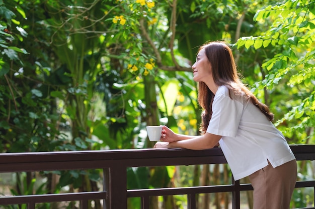 Photo portrait image of a beautiful young asian woman drinking coffee and relaxing on balcony at home