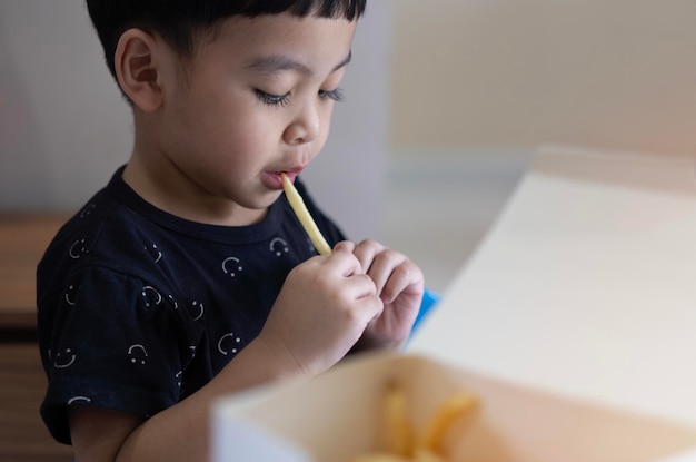 Portrait of small little cute Asian boy kid eating french fries at the table in the restaurant or at home