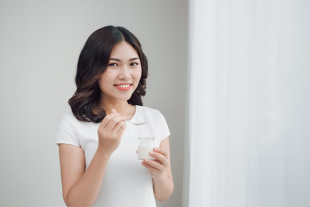 Portrait of young asian woman at home eating yogurt