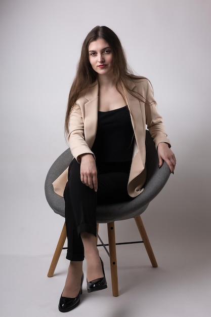 Portrait of a young brunette with long hair in the studio Cute girl sitting on a chair on a white background