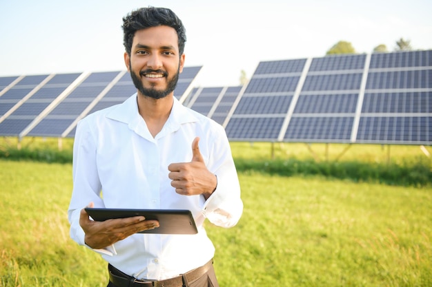 Photo portrait of young indian male engineer standing near solar panels with clear blue sky background renewable and clean energy skill india copy space