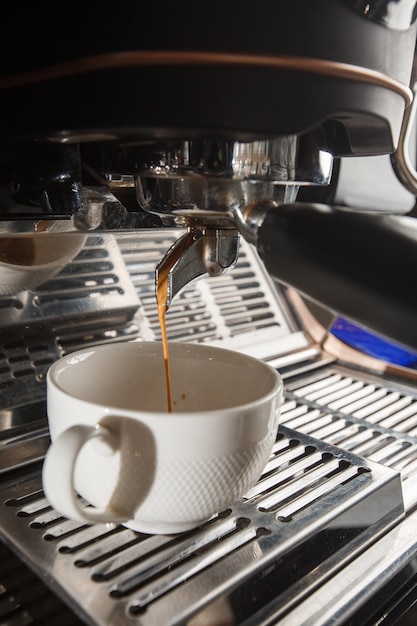 Pouring coffee stream from professional machine in cup Barista making espresso using filter holder Flowing fresh ground coffee