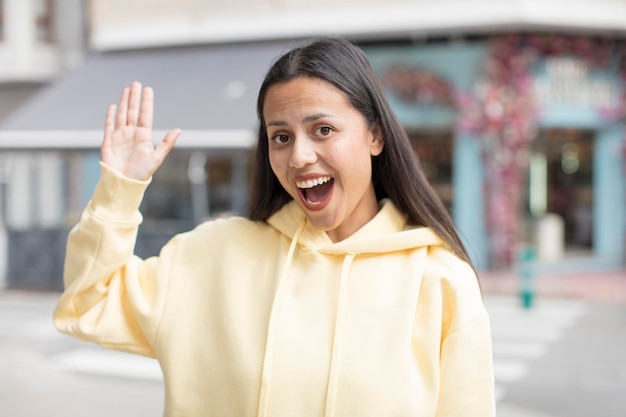 Photo pretty hispanic woman smiling happily and cheerfully waving hand welcoming and greeting you or sayin