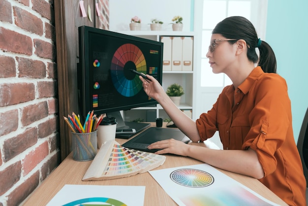 Foto operaia grafica femminile piuttosto professionale che utilizza la penna del pad digitale che punta lo schermo del computer e pensa a come progettare un nuovo prodotto nell'ufficio dell'azienda.