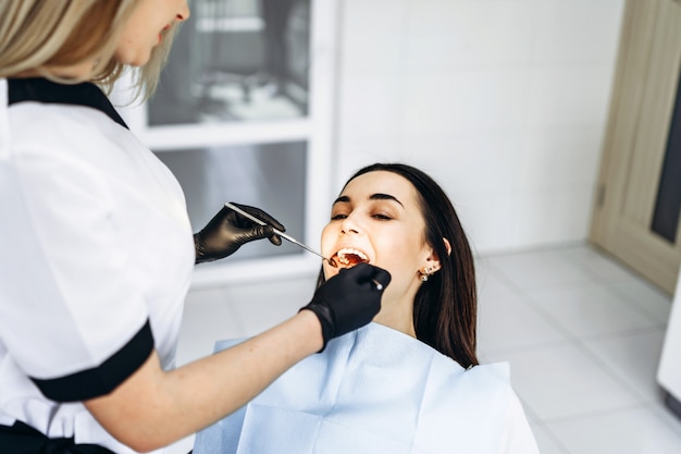 Pretty young female dentist making examination and treatment for young female patient in dental clinic.