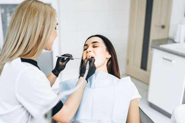 Pretty young female dentist making examination and treatment for young female patient in dental clinic.