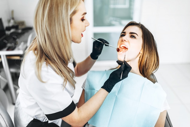 Pretty young female dentist making examination and treatment for young female patient in dental clinic.