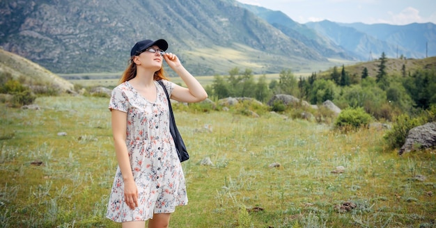 Pretty young woman in cap and short dress admires the beautiful view in mountains Hiking outdoor activities summer vacations of female student