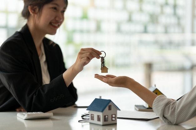 Photo real estate agent holding house key to his client after signing contract agreement in officeconcept for real estate moving home or renting property