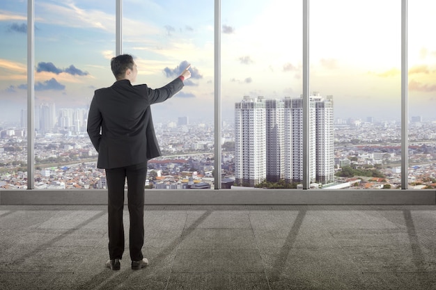 Rear view of Asian businessman pointing through the window on the office room