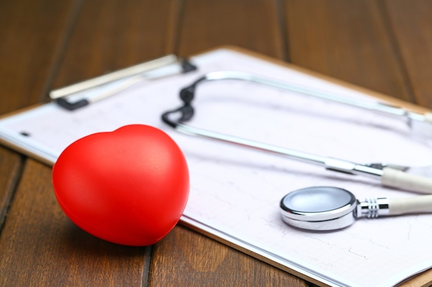 Red heart with stethoscope and electrocardiogram on wooden background