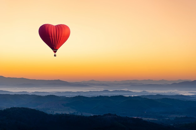 Red hot air balloon in the shape of a heart flying over the mountain