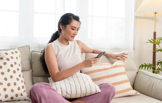 Relaxed smiling asian woman on the couch at home she is using a smartphone and texting