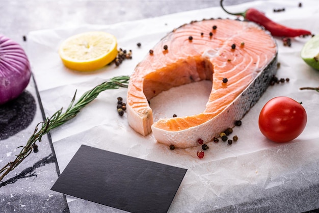 Salmon steak, red fish lies on parchment paper, next to lemon pepper tomato and herbs