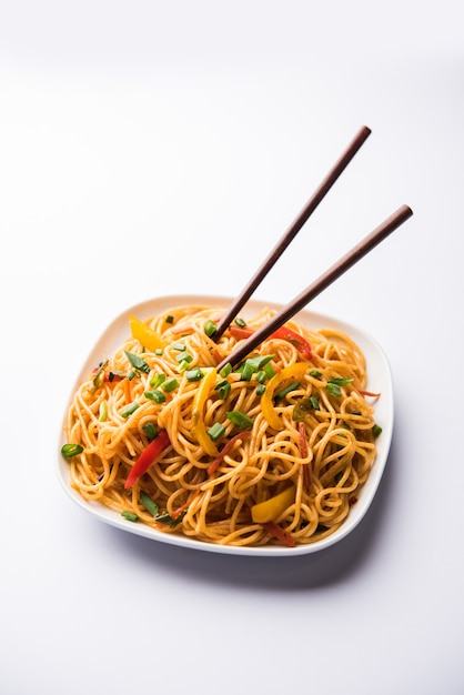 Schezwan Noodles or vegetable Hakka Noodles or chow mein is a popular Indo-Chinese recipes, served in a bowl or plate with wooden chopsticks. selective focus