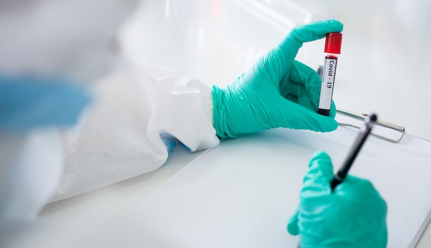 Scientists and microbiologists with PPE suit and face mask hold test tube with blood collected from patients covid19, to create vaccine for coronavirus.