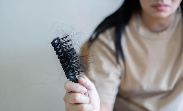 Selective focus Asian girl with a comb and problem hair on light beige background