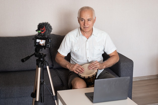 Senior man playing drum at home and recording video for blog