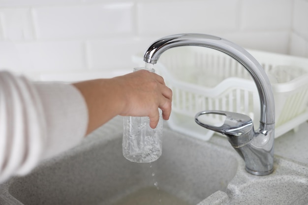 Photo separate waste collection at home a woman opens water in the kitchen sink and rinses plastic bottles for recycling caring for the environment proper disposal of household waste