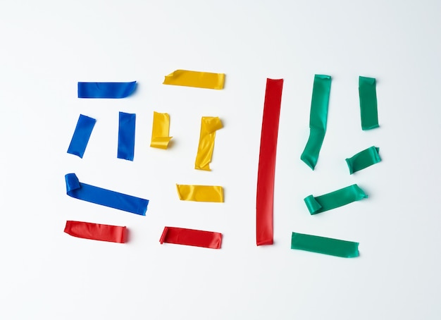 Set of torn multicolored rubber pieces of electrical tape glued to a white surface