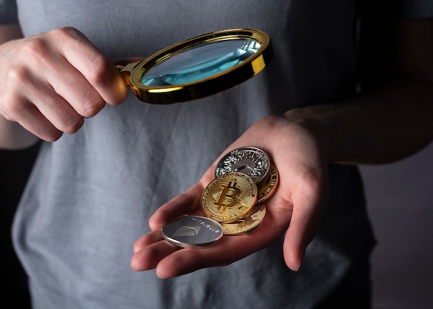 Shiny gold and silver coins of crypto currency in female hand palm with magnifying loupe close up. Pile of bitcoin and other cryptocurrency.