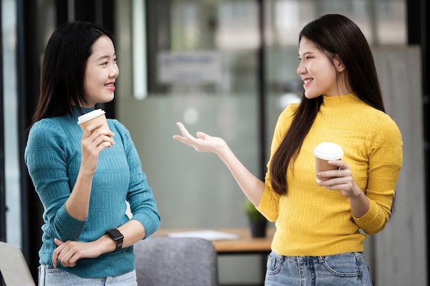 Foto scatto di due giovani donne sorridenti che parlano mentre bevono caffè sedute sul divano nel soggiorno dell'ufficio