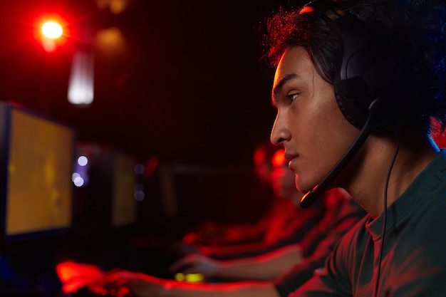 Side view of young gamer wearing headphones playing computer games with his friends