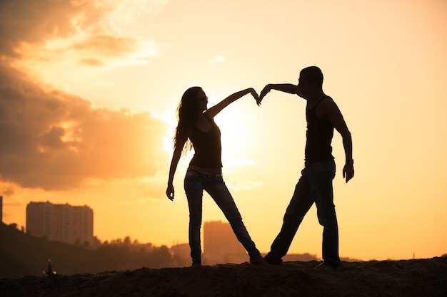 Silhouette of couple on a sunset making heart symbol