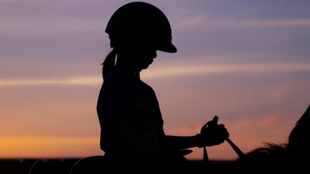 Silhouette image of school kid girl riding horse againts the twilight sky.