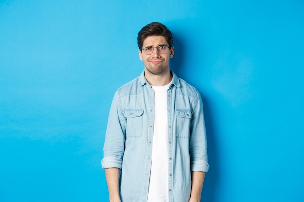 Skeptical and doubtful guy in glasses, looking confused at something strange, blue wall