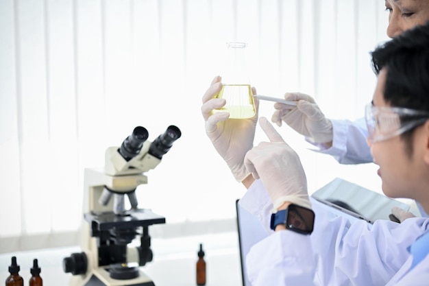 Photo a smart asian male scientist holding a conical beaker looking at the liquid sample