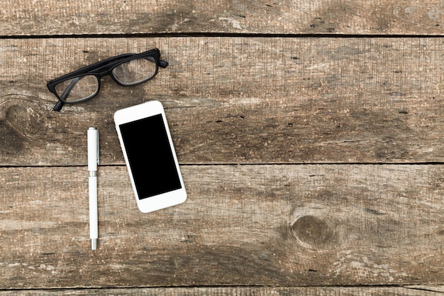 Smartphone with black screen, glasses and pen  on wooden table