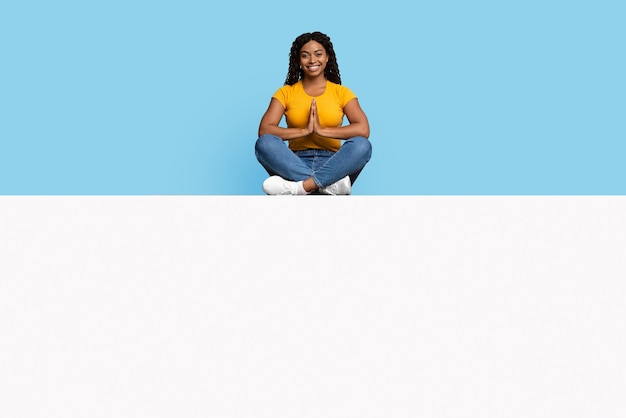 Smiling black lady with curly hair meditating on empty board