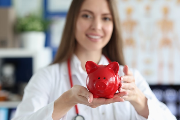 Smiling female doctor holding red pig piggy bank