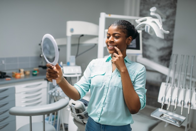 Smiling female patient looks on teeth in mirror